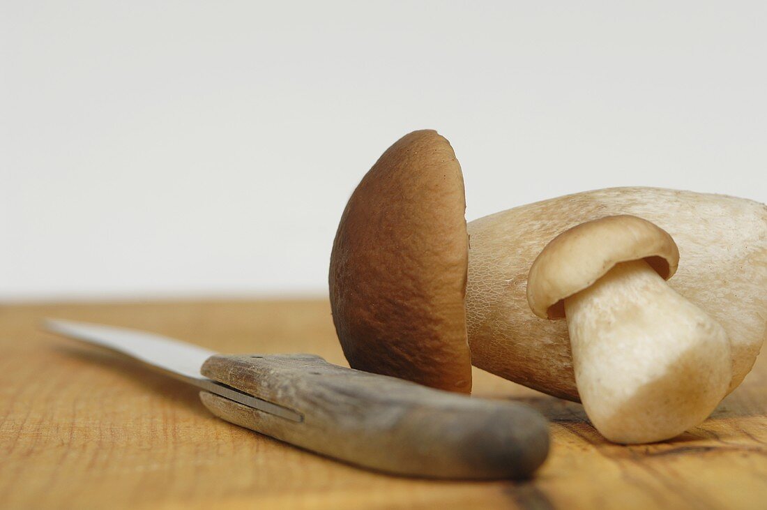 Two porcini mushrooms on a chopping board with a knife