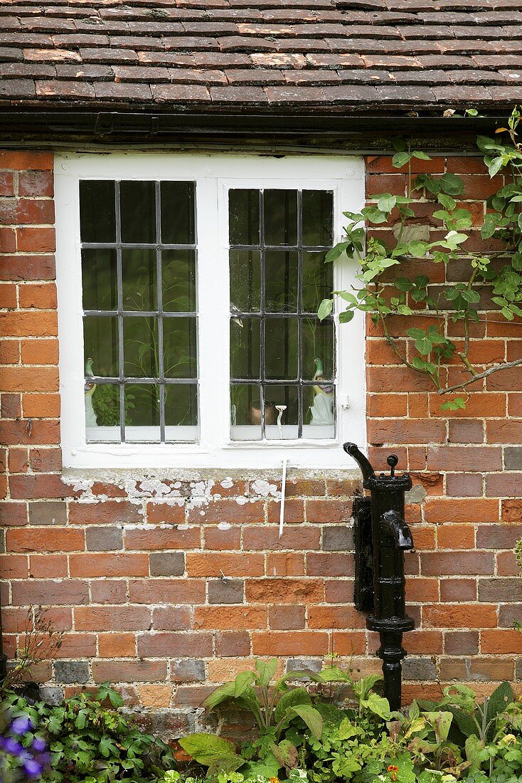 Brunnen mit Handpumpe unter Fenster eines englischen Landhauses