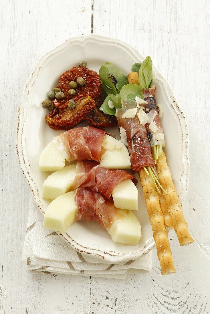 Antipasti platter with melon, ham, grissini and dried tomatoes