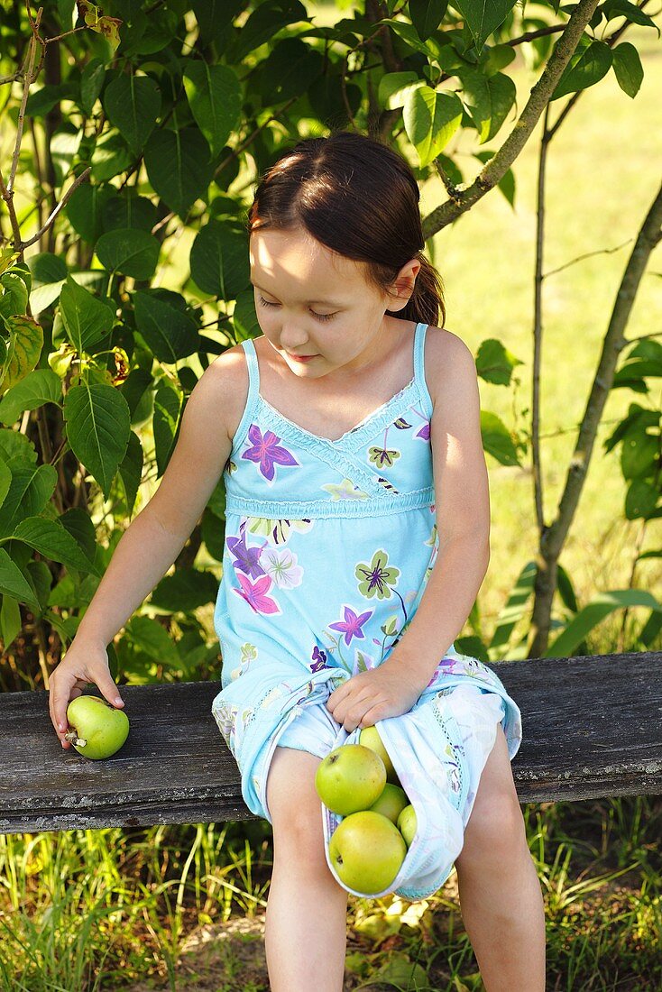 A girl sitting on a garden bench with green apples