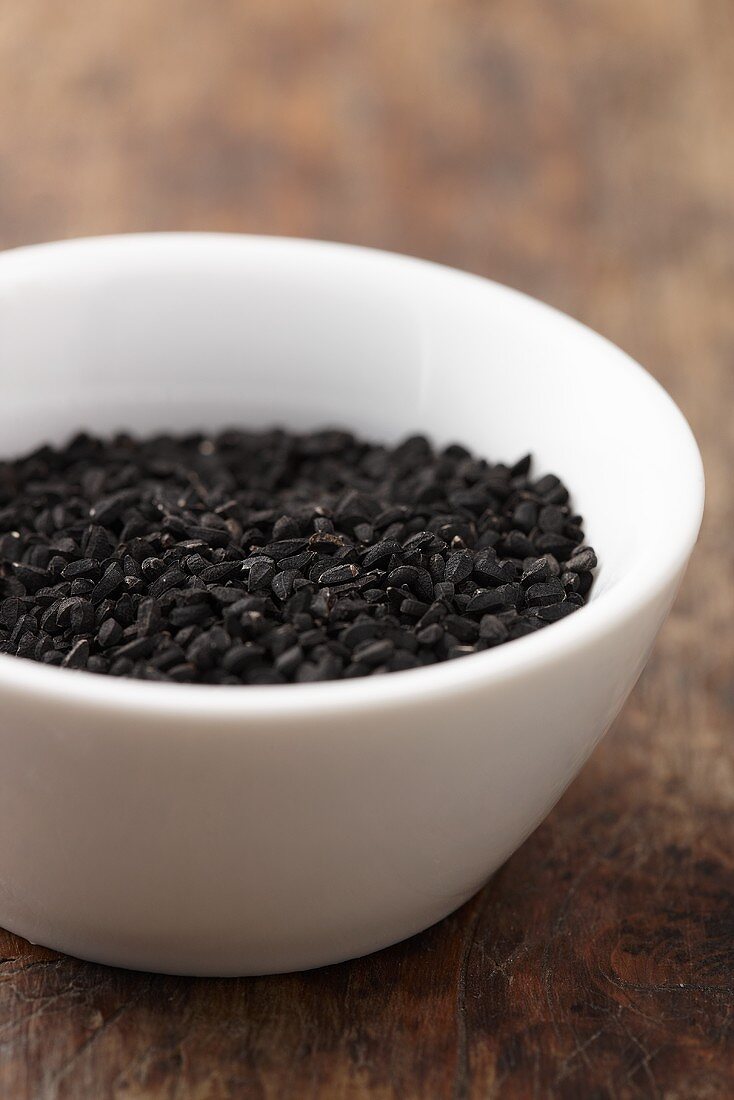 A bowl of black cumin on a wooden surface