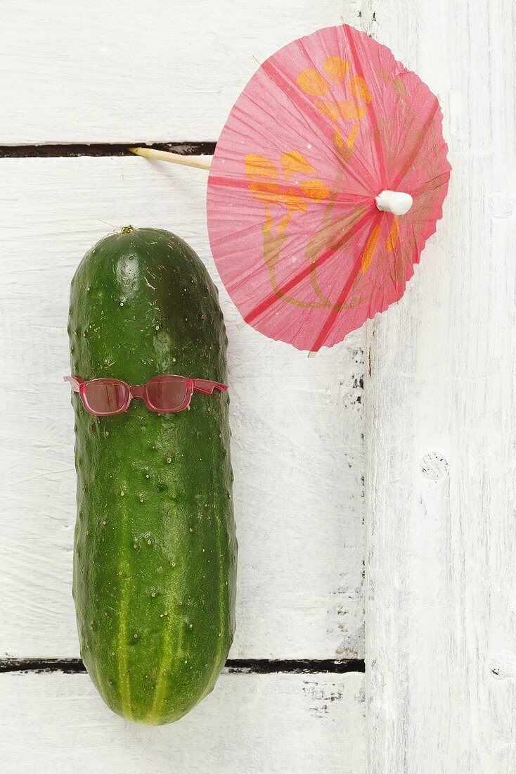 A cucumber with sunglasses and a cocktail umbrella