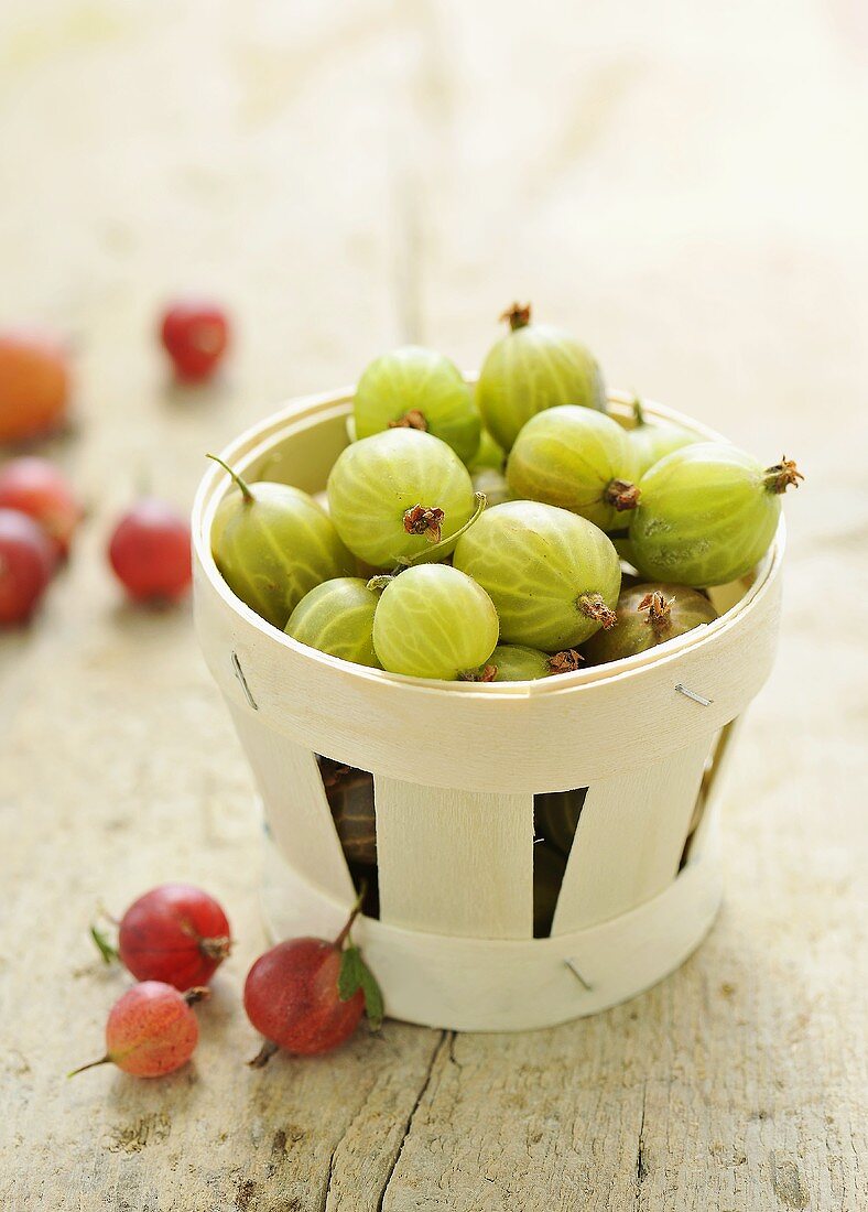 Gooseberries in a wooden basket and on a wooden surface