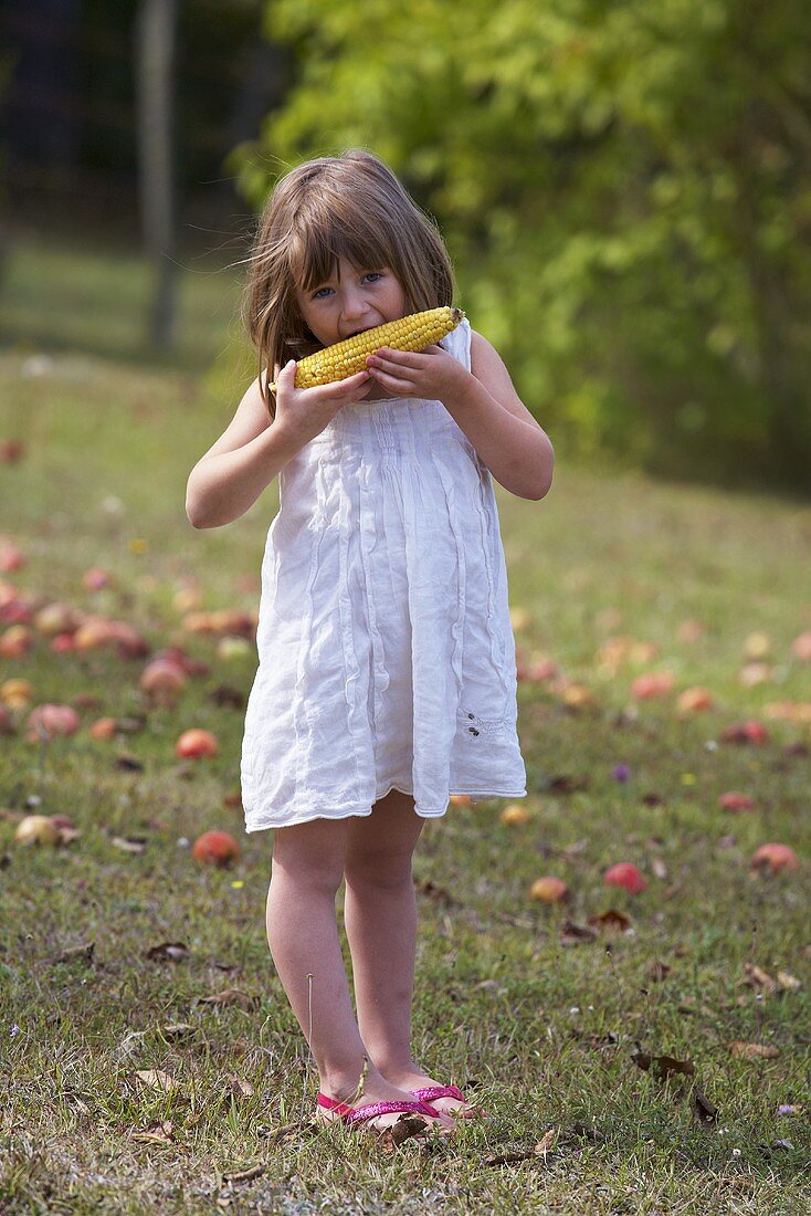 A girl eating a corn cob in a garden