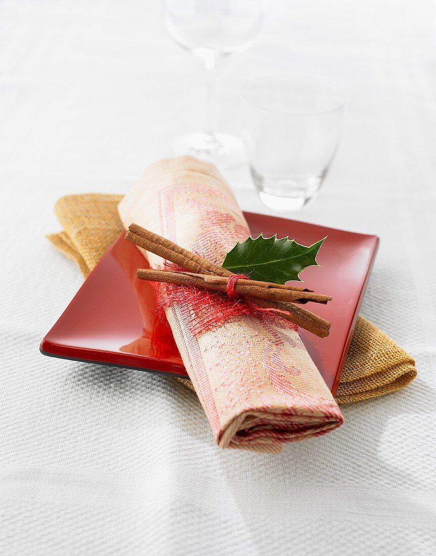 A place setting with cinnamon sticks and a holly leaf