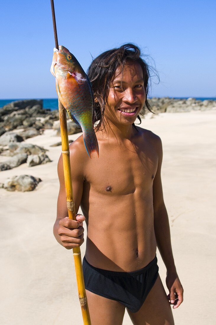 A young man with a speared parrotfish on a beach