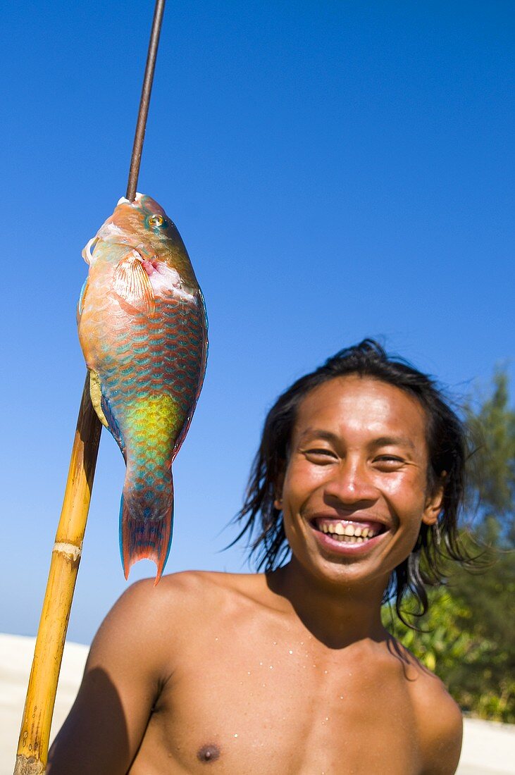Junger Mann mit aufgespiesstem Papageienfisch am Strand