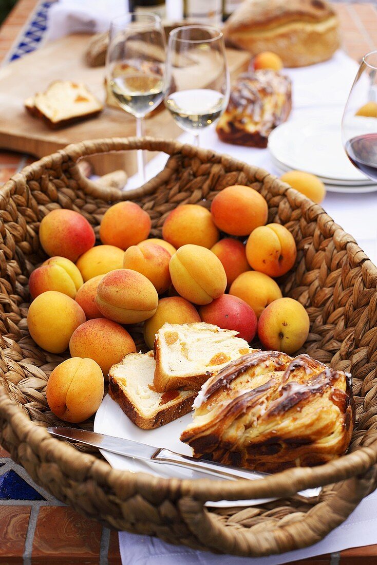 Aprikosenkuchen und frische Aprikosen im Korb, Weissweingläser