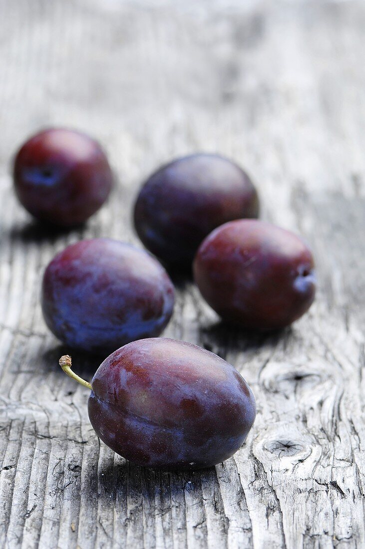 Five plums on a wooden surface