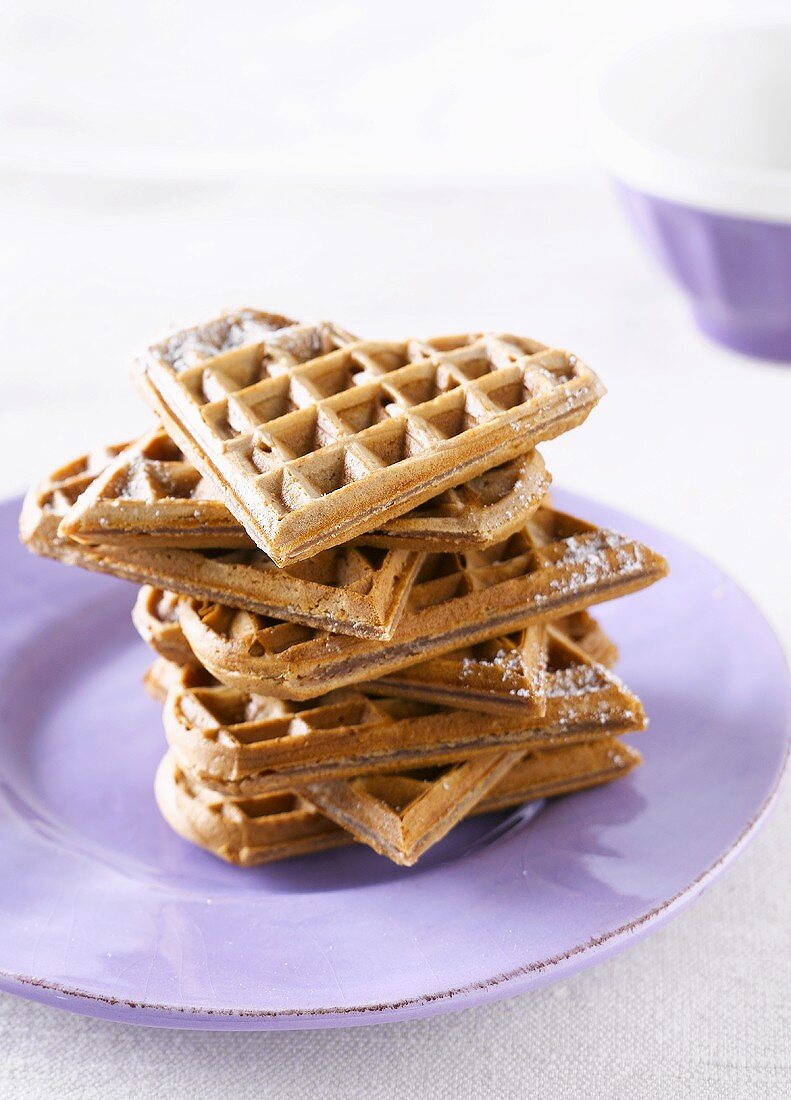 A stack of heart-shaped waffles with icing sugar