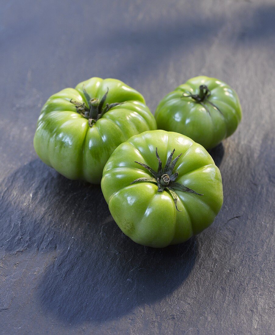 Three green tomatoes on a stone surface