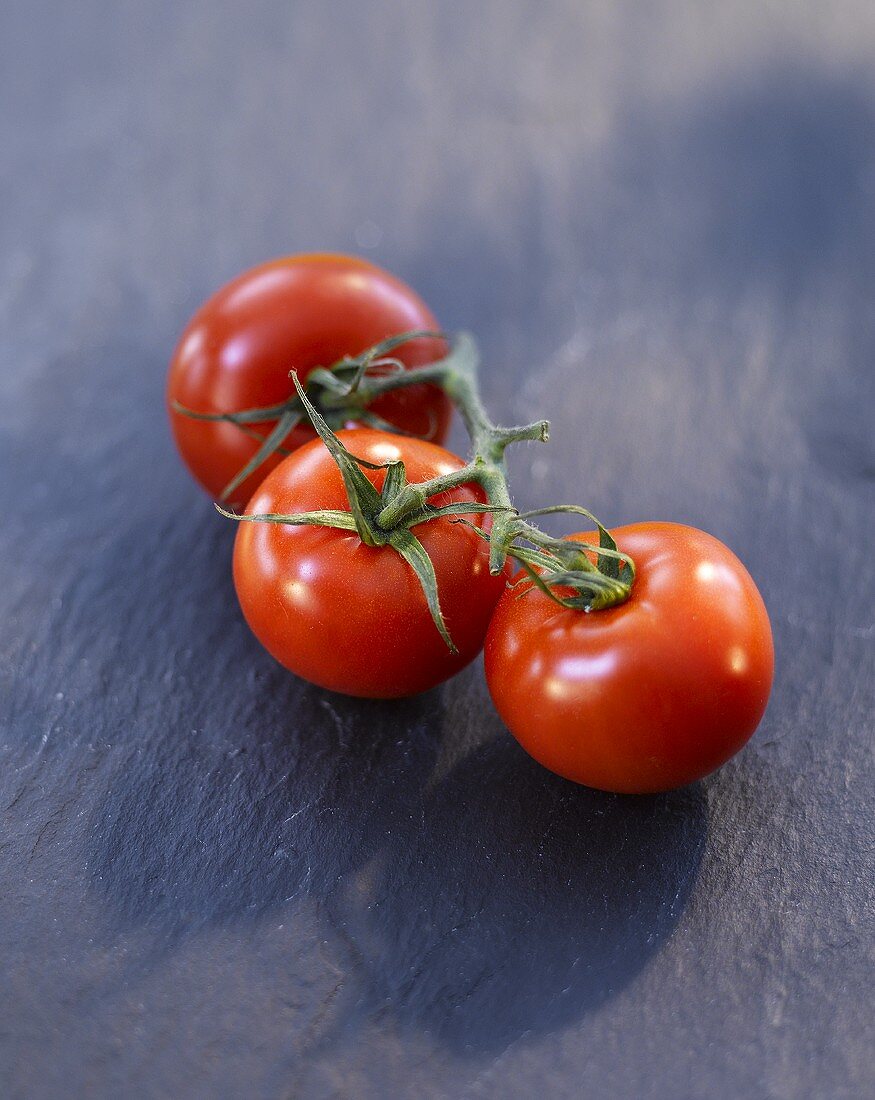 Three tomatoes on a stone surface