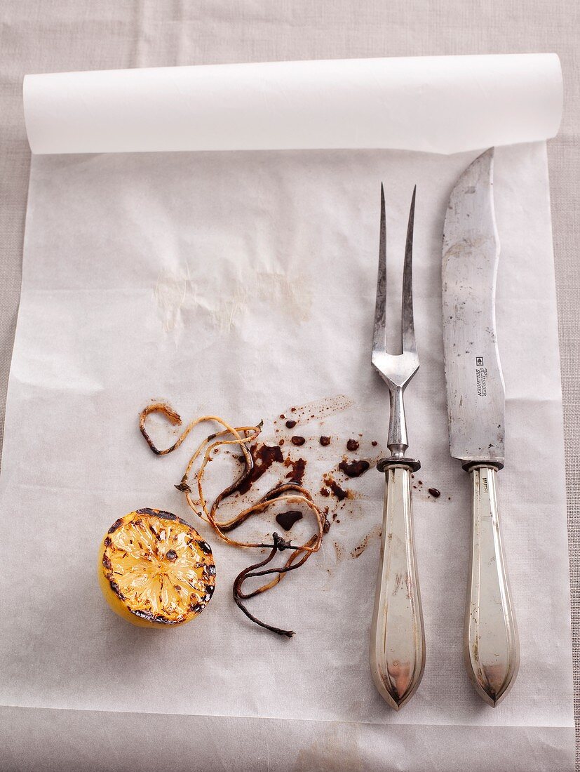 Parchment paper with a carving knife and fork, grilled lemons and twine