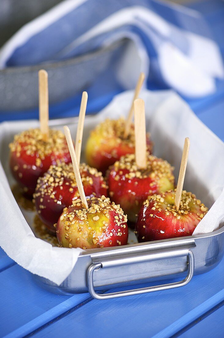Toffee apples covered with chopped nuts in a pan