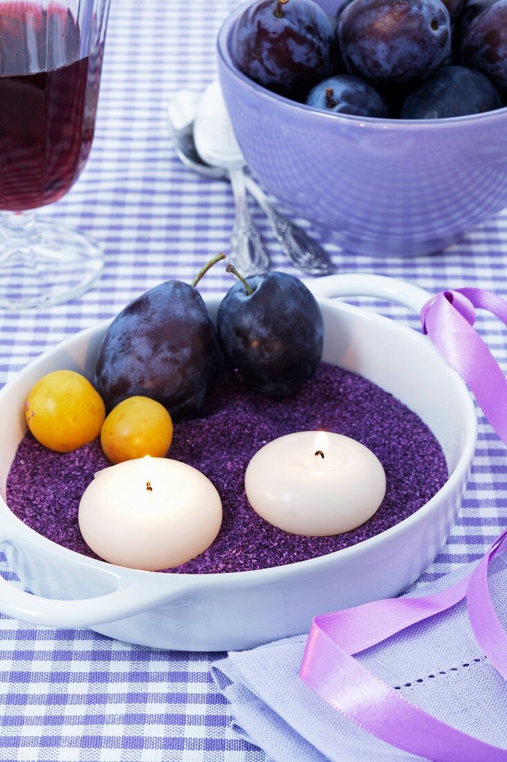 Candles, damsons and greengages on purple sand