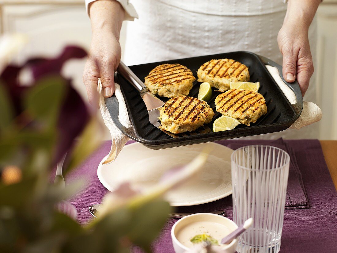 Female chef holding grill pan containing fish cakes