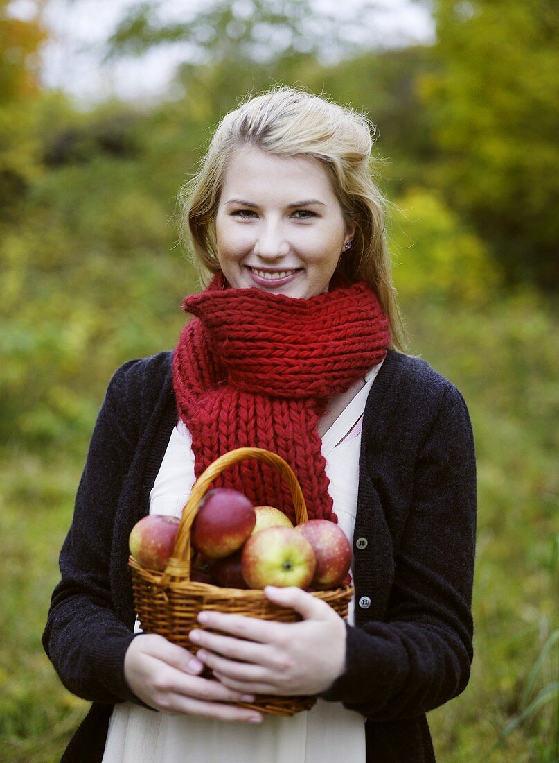 Frau hält Korb mit frisch geernteten Äpfeln