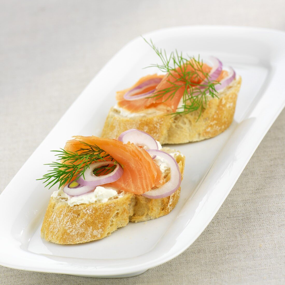 Baguette slices topped with smoked salmon, onions and dill