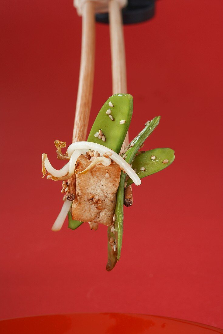 Gebratenes Tofu mit Sesam-Zuckerschoten zwischen Essstäbchen