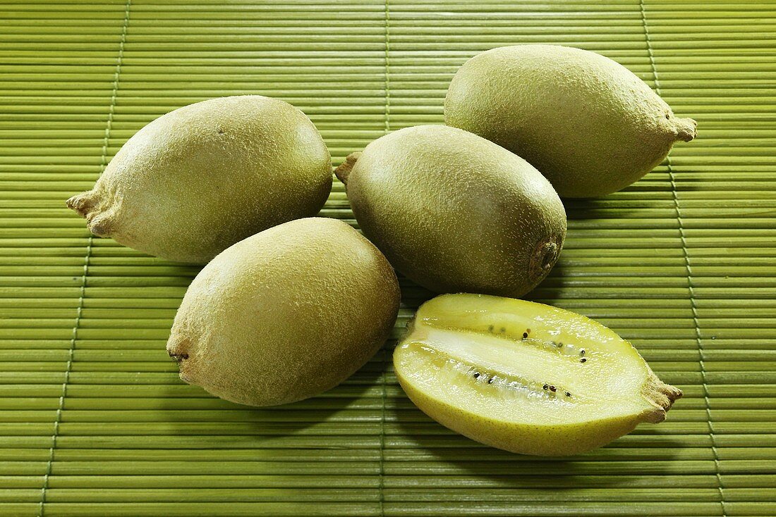 Several whole kiwi fruits and one half on a bamboo mat