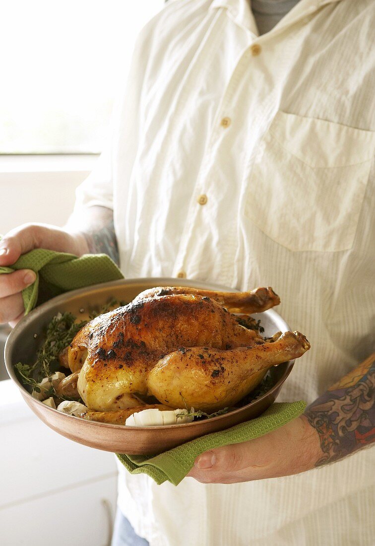 Man holding roast chicken in pan