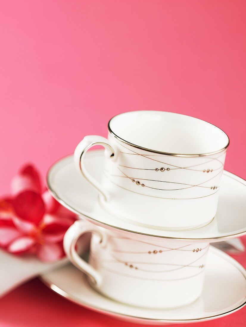 Two stacked teacups and saucers against pink background