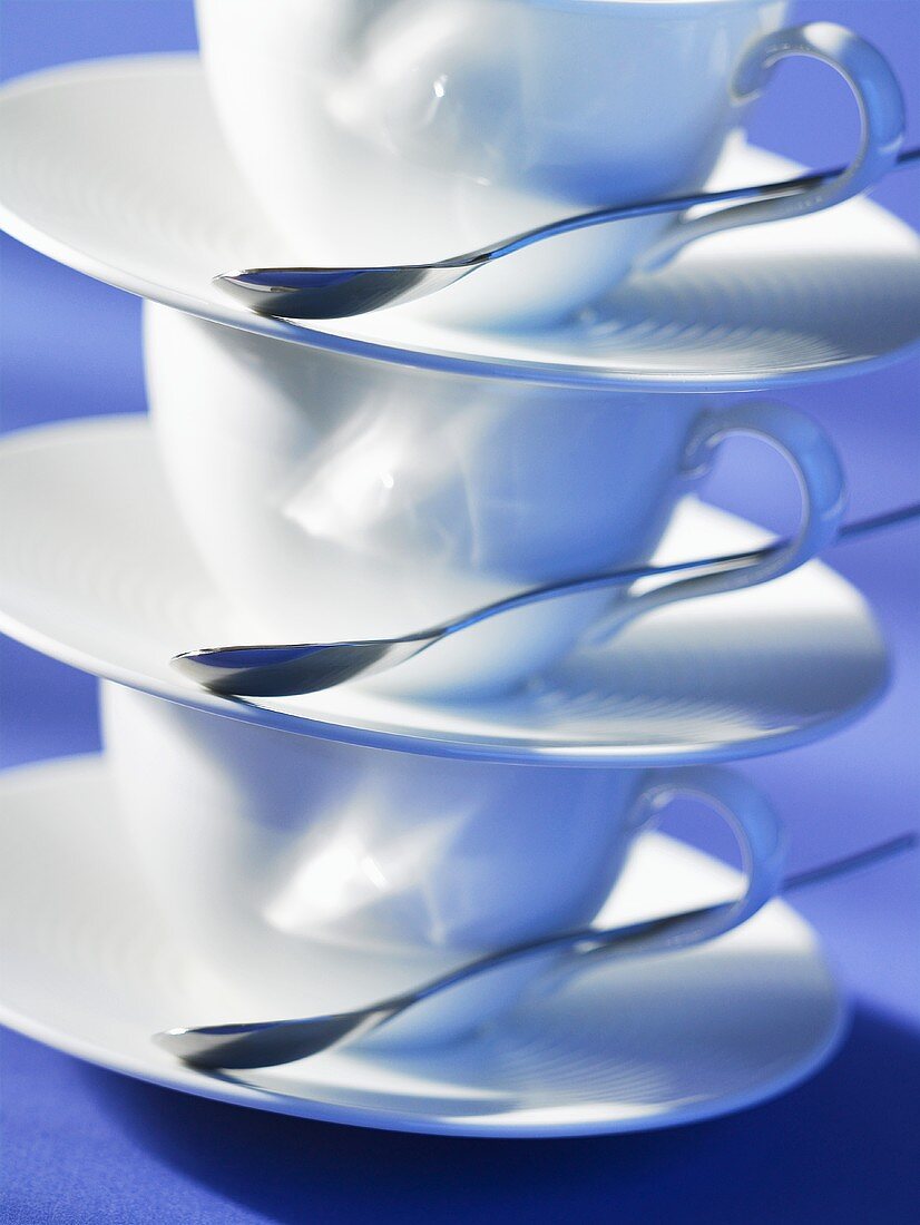 Three stacked coffee cups and saucers with spoons