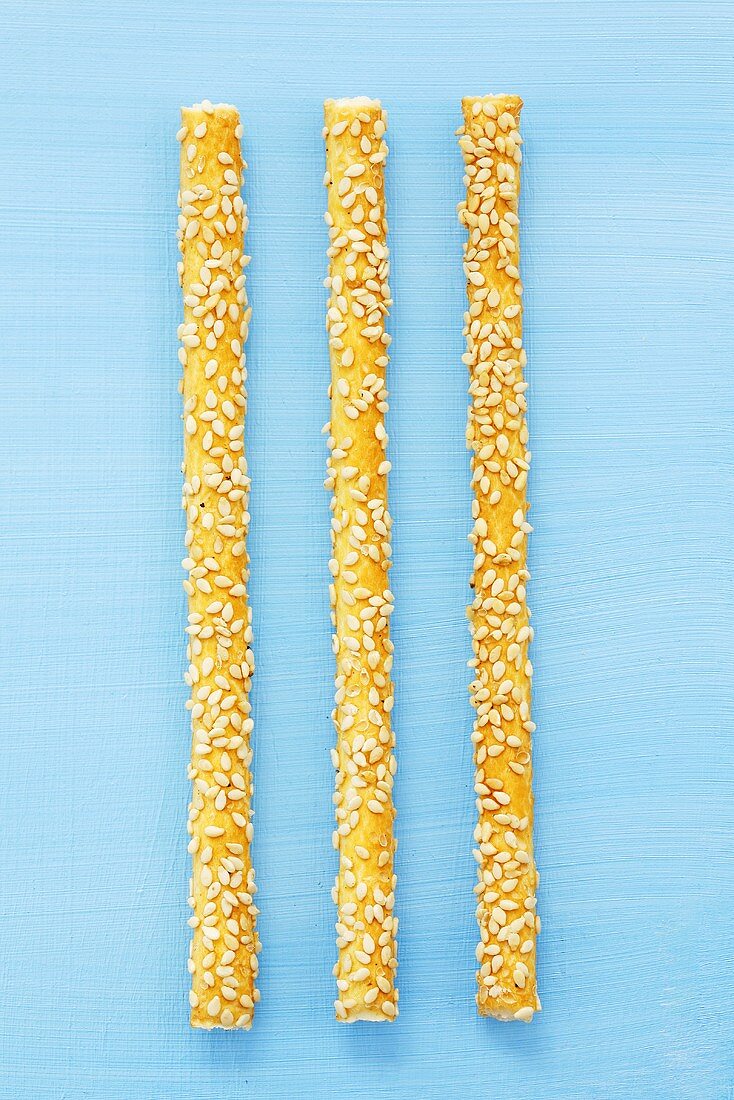 Three sesame grissini on blue background