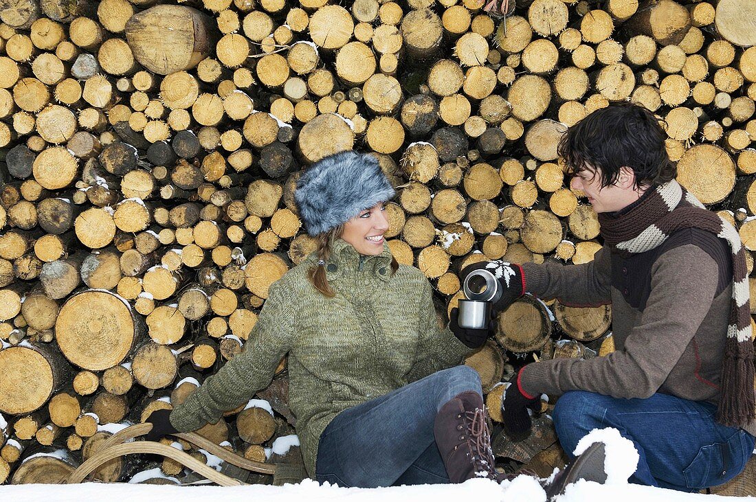 Junges Paar sitzt mit Thermoskanne am Holzstapel