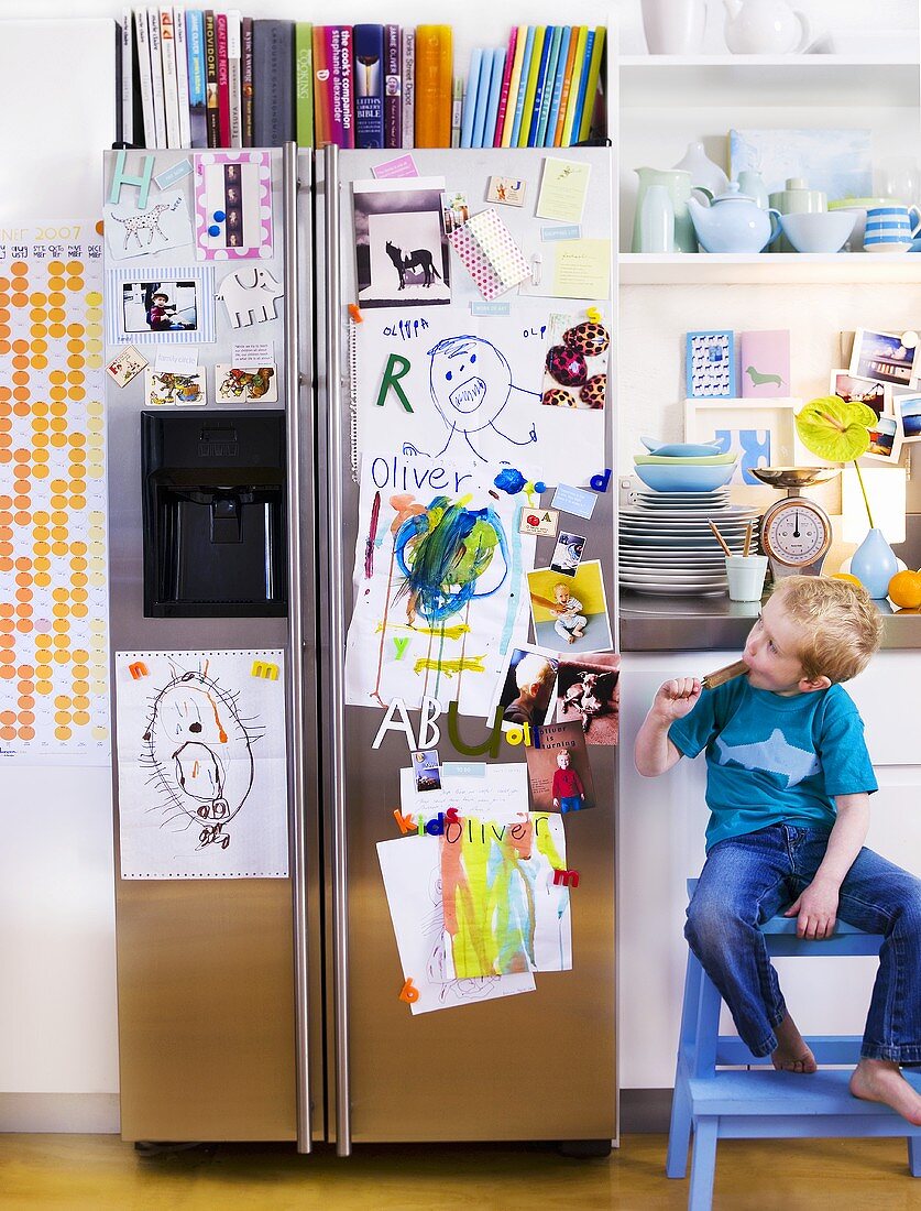 Kleiner Junge in Küche neben Kühlschrank mit Kinderbildern