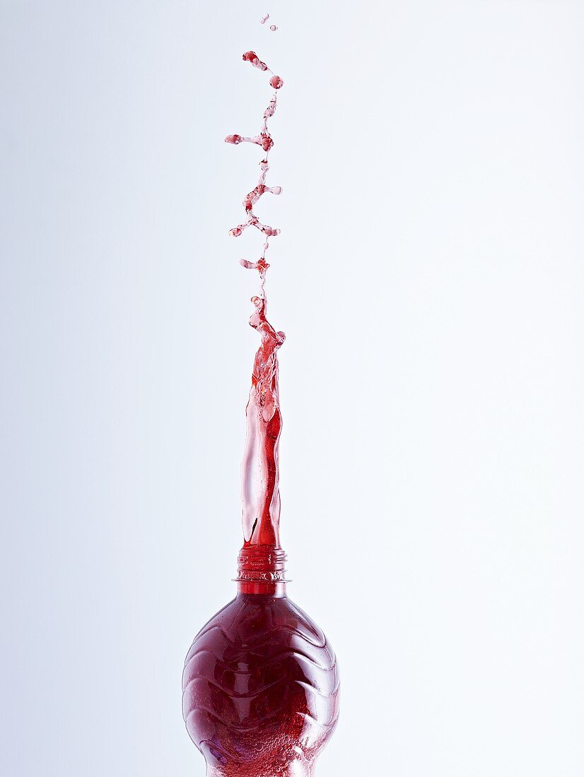 Cherry juice splashing out of a bottle