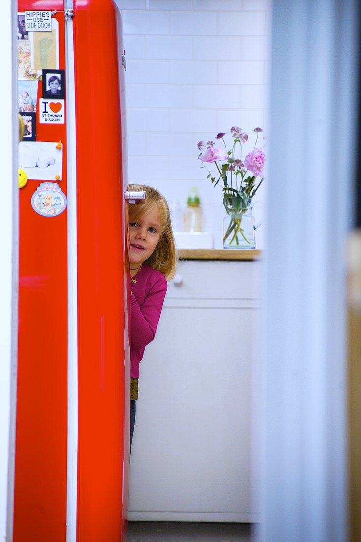 Kleines Mädchen versteckt sich hinter Kühlschrank