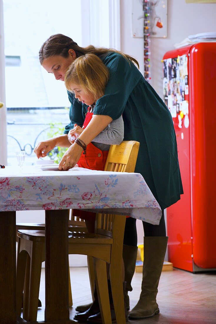 Mutter und kleine Tochter decken Esstisch in der Küche