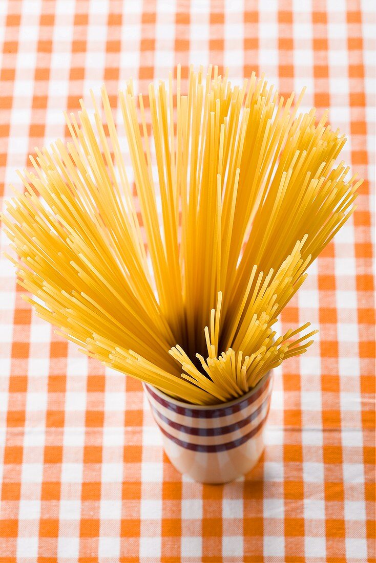 Spaghetti in beaker on checked tablecloth