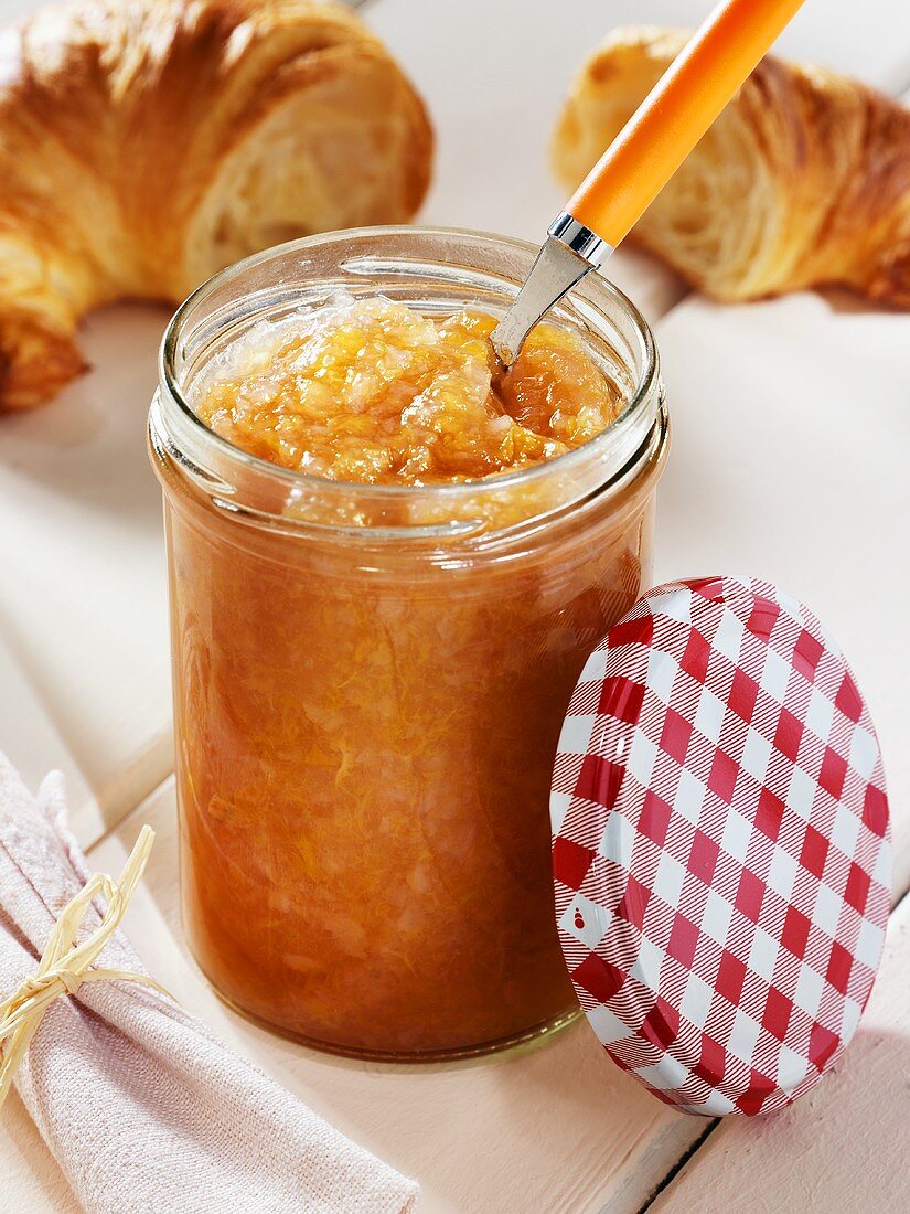 Pear and peach jam in jar in front of croissant