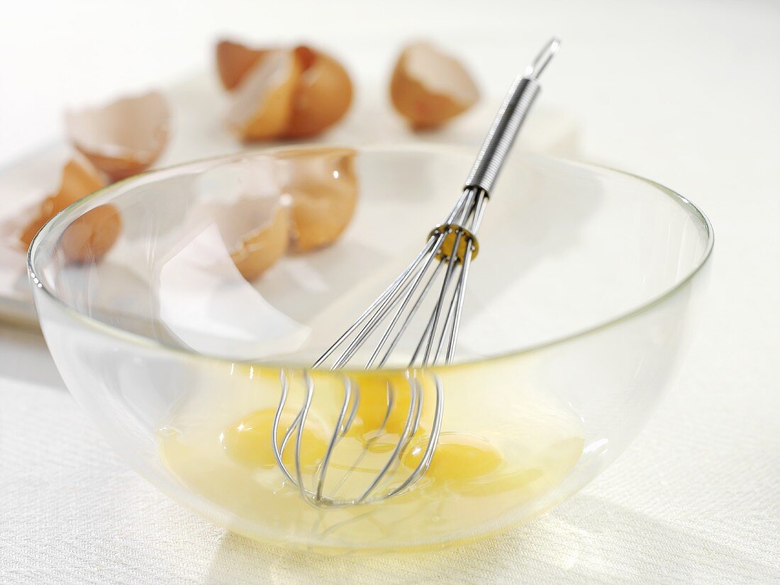 Eggs broken into glass bowl with whisk