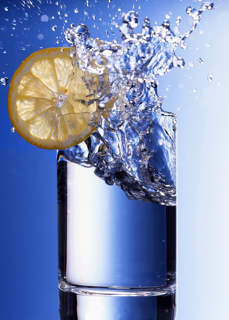 Water splashing out of glass with slice of lemon