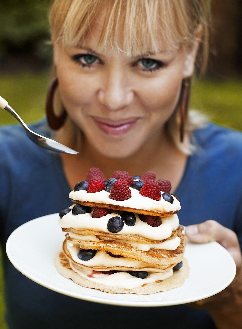 Frau isst Pancakes mit Sahne und Beeren