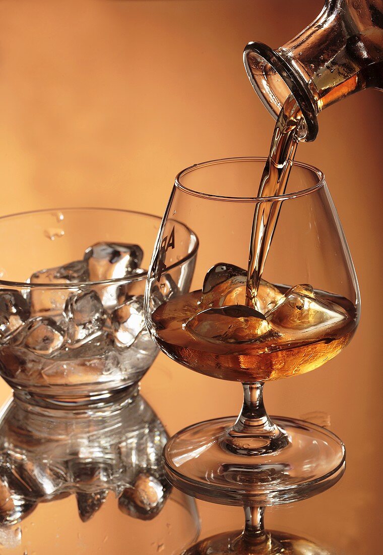 Pouring brandy into a glass containing ice cubes