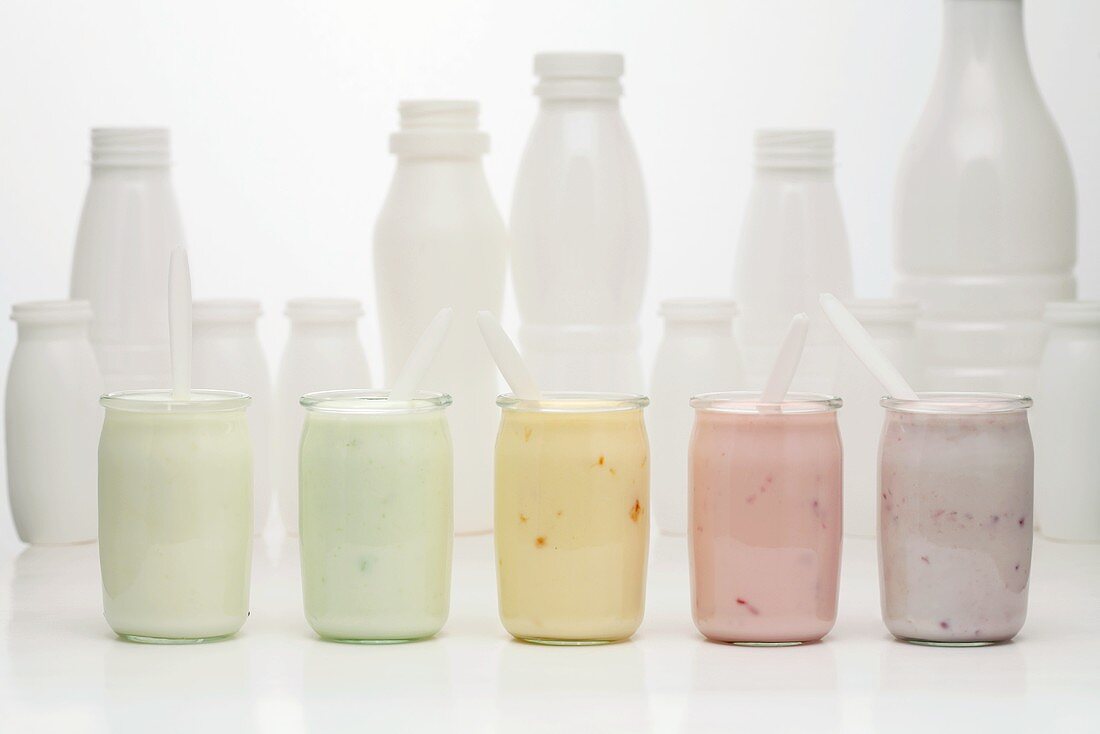 Verschiedene Joghurtgläser vor Plastikflaschen