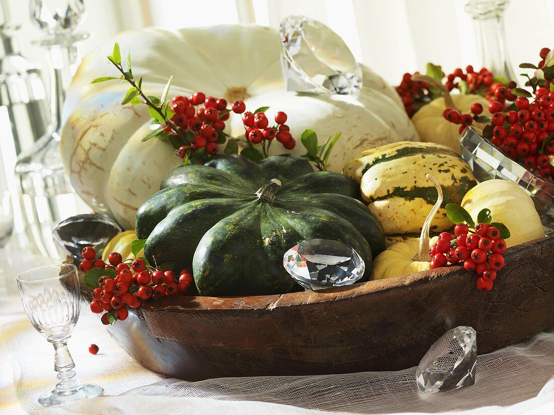 A wooden bowl filled with pumpkins and firethorn berries as autumnal decoration