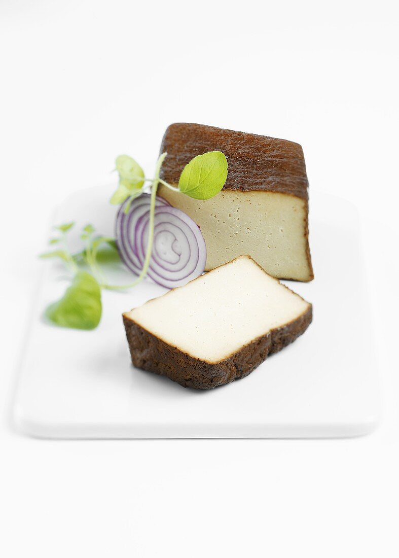 Geräucherter Tofu, angeschnitten, mit roter Zwiebel und Oregano auf Porzellanplatte