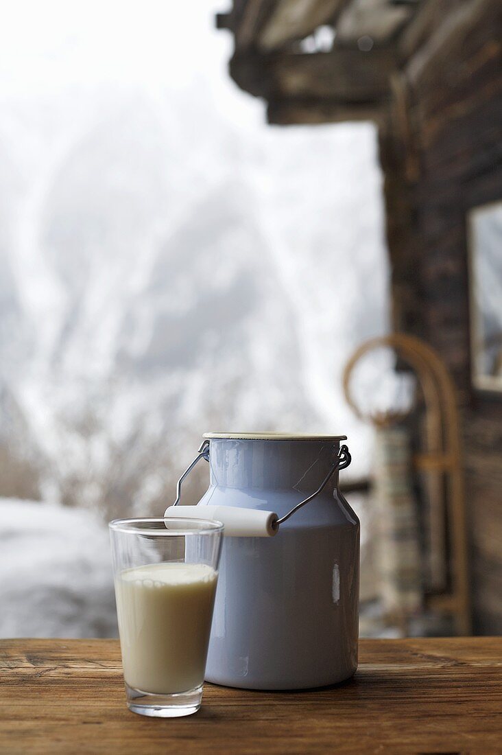 Milchkanne und Milchglas auf Tisch vor Almhütte