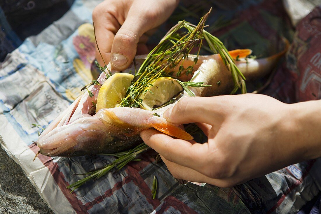 Hands holding smoked bass stuffed with lemon, thyme and rosemary