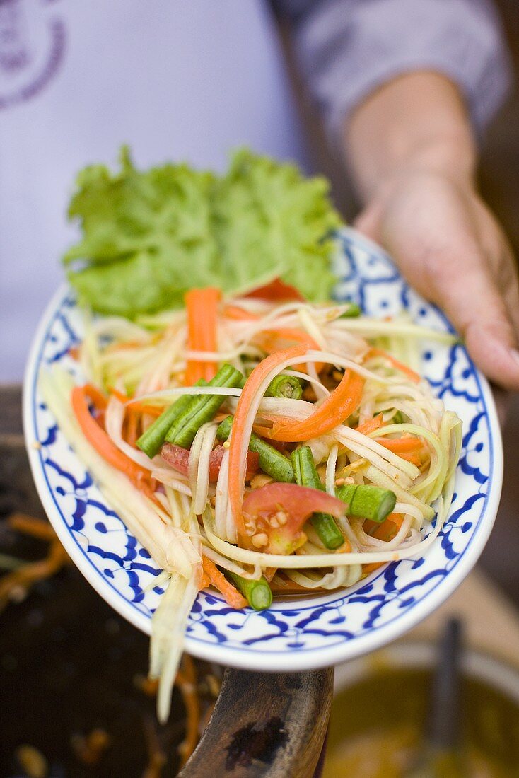 Hand hält Teller mit Gemüsesalat (Thailand)