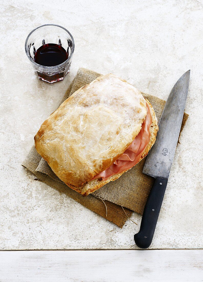 Ham-filled ciabatta, glass of red wine, knife