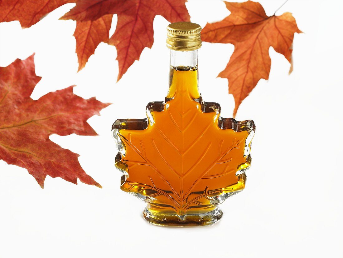 A bottle of maple syrup in shape of maple leaf with red maple leaves