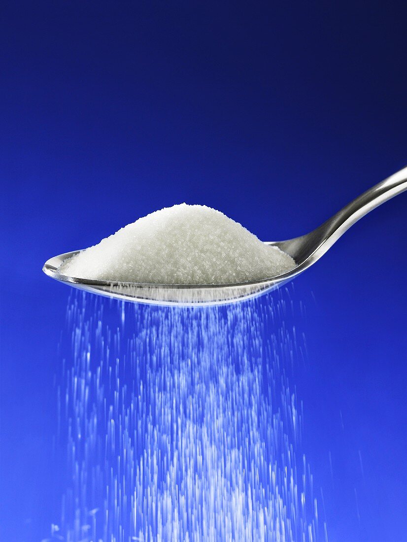 Salt trickling from spoon against blue background