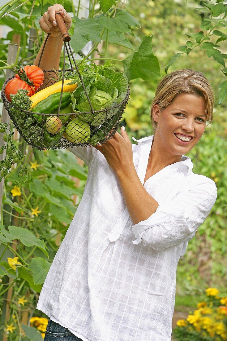 Woman holding wire basket of organic vegetables in garden