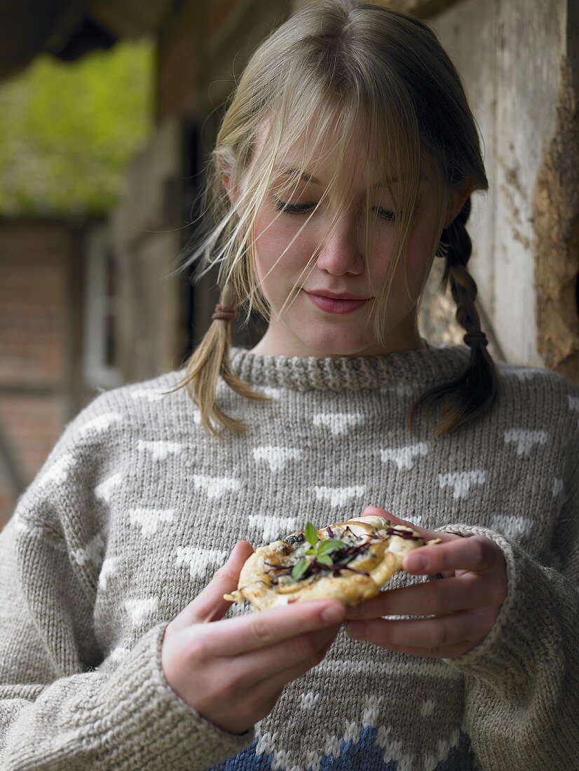 Young woman eating pizzette with pear, radicchio & Gorgonzola